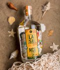 LA SU MGO Flasche im Sand zwischen Muscheln und Fischernetz