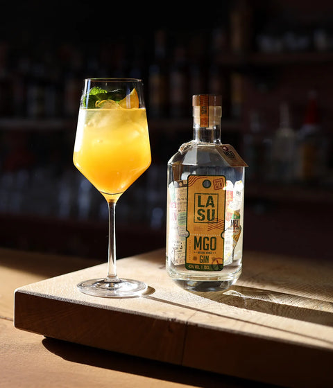 LA SU MGO Gin mit Cocktailglas auf Holzbrett, Bar-Ambiente im Hintergrund