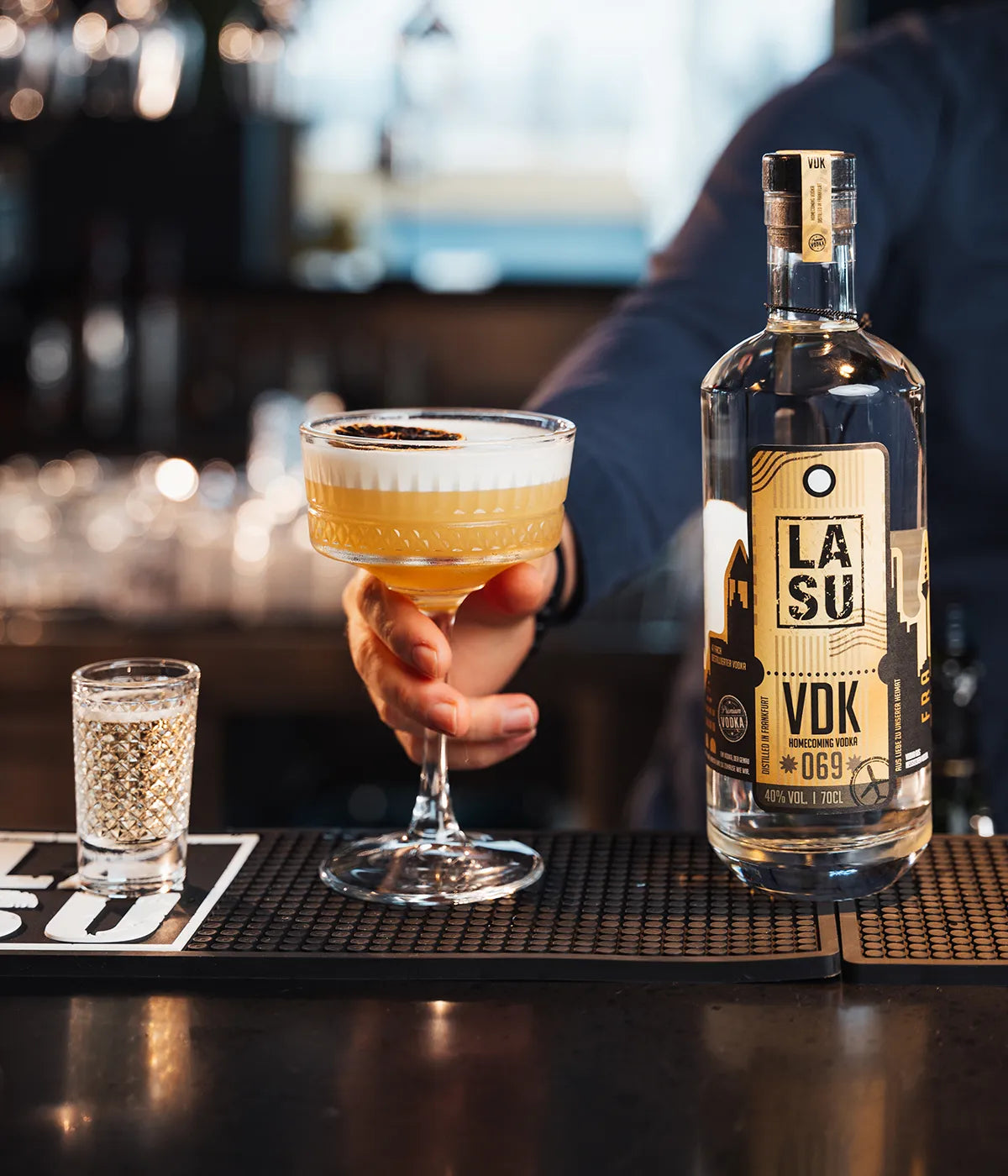 Bartender serviert LA SU VDK Cocktail mit Espuma und Shot an der Bar