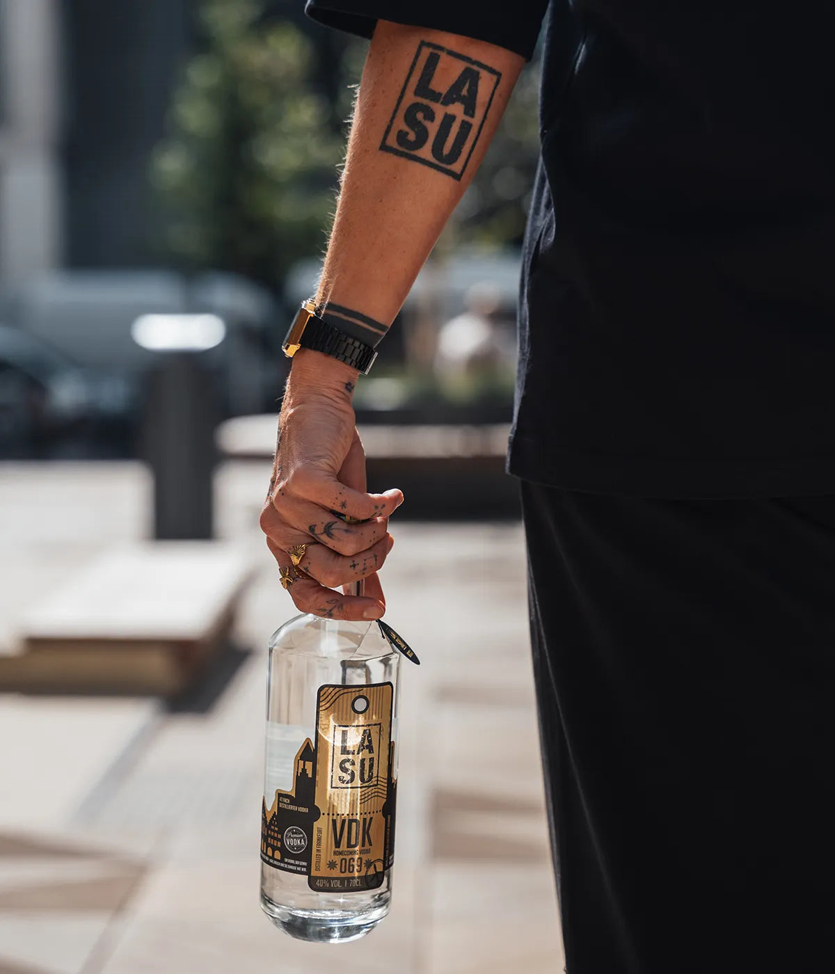 Person mit LA SU Tattoo am Arm trägt VDK Flasche in der Stadt